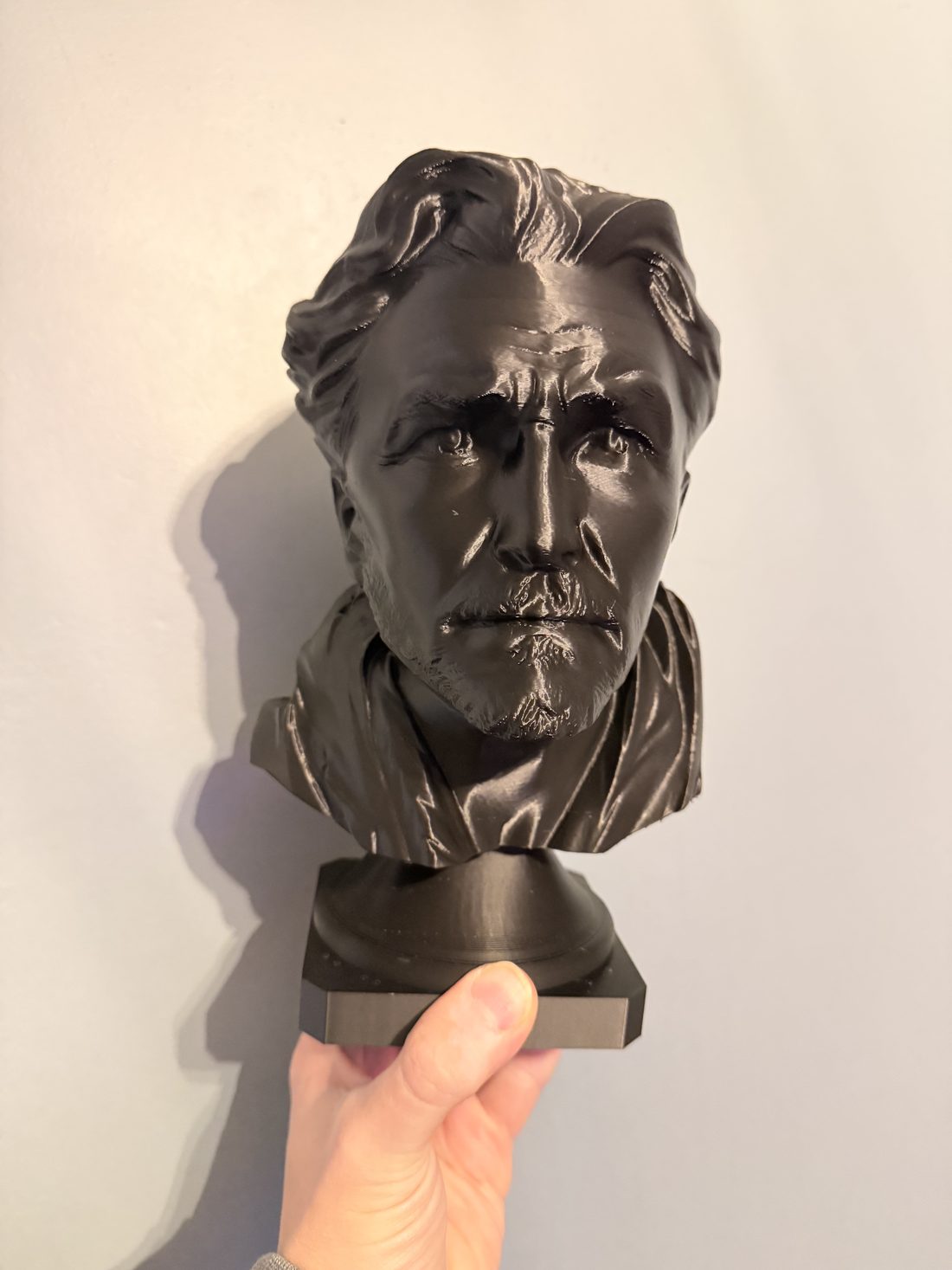Black-finish bust of a bearded man with swept-back hair, held in one hand