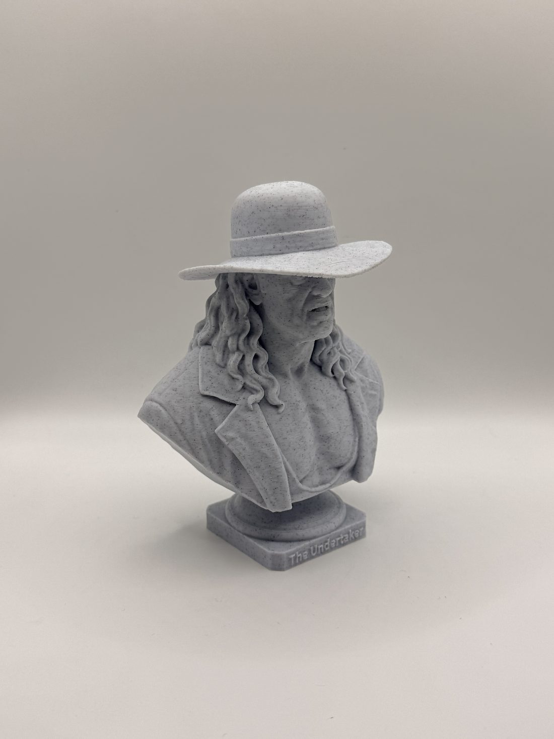 Marble-look bust of a wrestler in a wide-brimmed hat and long coat, with long hair