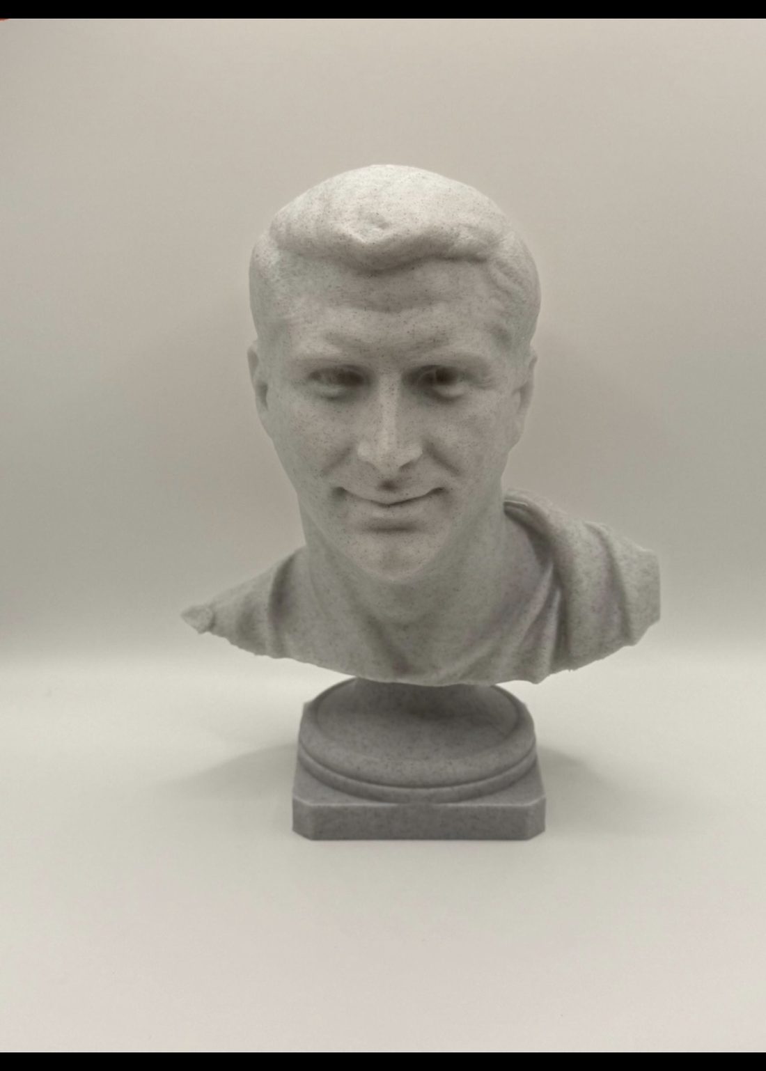 Marble-look bust of a smiling man with short hair, on a round plinth